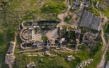 Hierapolis Antik Kenti ve Türkiye 'nin Denizli kentindeki ünlü Pamukkale travertinlerinin insansız hava aracı görüntüsü, yukarıdan antik harabeleri, Roma tiyatrosunu, sütunları ve manzarayı gösteriyor.