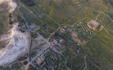 Hierapolis Antik Kenti ve Türkiye 'nin Denizli kentindeki ünlü Pamukkale travertinlerinin insansız hava aracı görüntüsü, yukarıdan antik harabeleri, Roma tiyatrosunu, sütunları ve manzarayı gösteriyor.