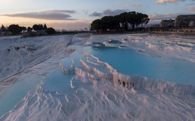 Türkiye 'nin Denizli kentindeki ünlü Pamukkale travertinlerinin ve termal havuzlarının insansız hava aracı görüntüsü, yukarıdan beyaz kalsiyum teraslarını, doğal oluşumları ve manzaralı manzaraları gösteriyor.