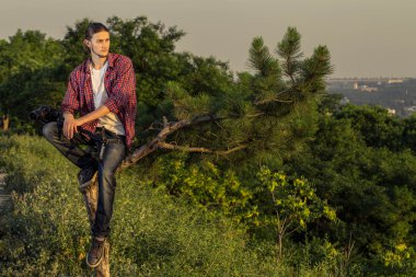 Ağaç üzerinde oturan genç fotoğrafçı.