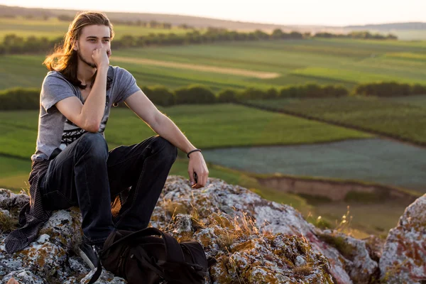 Beau jeune homme assis sur un rocher . — Photo