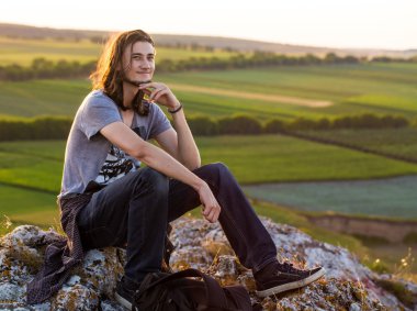 Kayalar üzerine oturan yakışıklı genç adam.