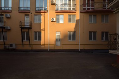 Işık ve gölge bir evin ön cephesini çiziyor. Binanın önünde pencereler, havalandırma ve asfalt alan var..