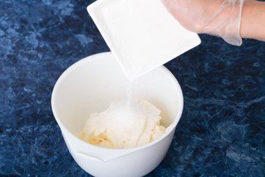 Sugar is poured into the cream cheese. Cheesecake making process. Blue marble background. Close-up.