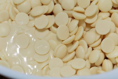 The pieces or granules of white chocolate are melted. Confectionery white chocolate. It occupies the entire surface of the image. Close-up.