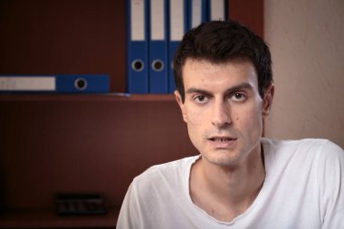 Yoğunlaşmış genç bir adamın portresi. Fotoğraf ofiste çekildi ve arka planda klasörler var. Yakın plan..