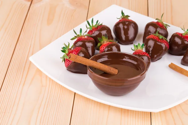 Strawberries in chocolate with cinnamon on wood. — Stock Photo, Image