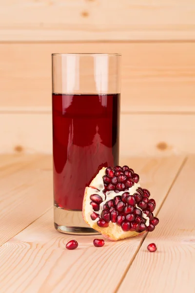 Glass of pomegranate juice and grains on wood. — Stock Photo, Image