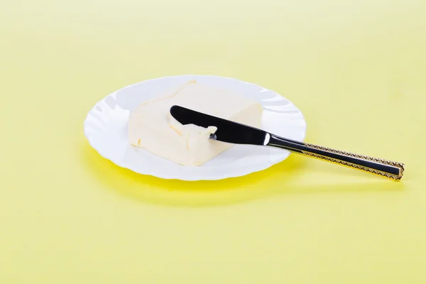 Pezzo di burro su piatto bianco con coltello . — Foto Stock