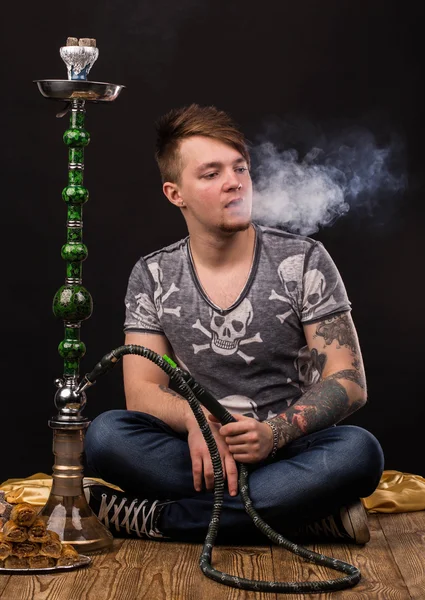 Tattooed man smoking traditional hookah. — Stock Photo, Image