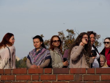 Neşeli arkadaşlar geniş bir gökyüzünün altında kırmızı tuğladan tarihi bir duvara bakıyor ve dinleniyorlar..