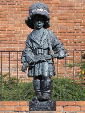 Küçük isyancı heykelinin yakın çekimi, çocuğun resmi yüzünü ve büyük askeri miğferi vurguluyor..