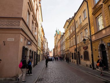 Turistler ve yerel halk Polonya 'nın Varşova Eski Kasabası' ndaki renkli kasaba evleriyle çevrili tarihi dar kaldırım taşları caddesinde yürüyorlar..