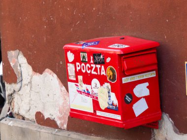 Polonya Post 'un (Poczta) Avrupa' da yıpranmış kırmızı bir duvardaki çıkartmalarla kaplı açık kırmızı posta kutusu..