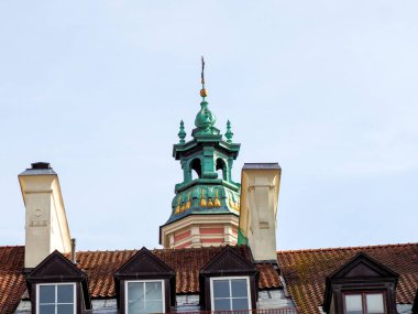 Varşova 'daki tarihi binaların kiremitli çatılarının üzerinde süslü yeşil bir kilise kulesi yükseliyor..