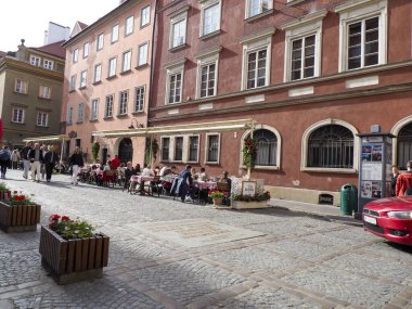 Turistler Varşova 'nın tarihi binalarının yakınındaki kırmızı şemsiyeli bir kafede yemek yemekten hoşlanıyorlar..