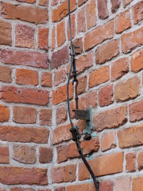 Tarihi bir binanın kırık kırmızı tuğla bir duvarına yakın plan büyük, koyu metal bir çapa ile onarılmış..