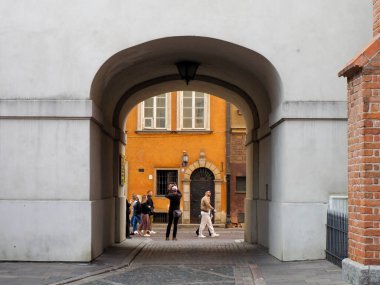 Turistler kırmızı tuğlalı bir duvarla büyük bir kemer yolundan geçerek parlak sarı bir avluya çıkıyorlar..