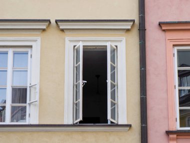 Tarihsel sarı ve pembe bir apartman cephesindeki açık beyaz pencere çerçevesinin yakın çekimi.