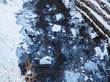 Kar ve kayalarla kısmen donmuş bir dağ nehri manzarası..
