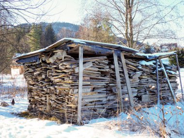 Dağları olan karlı bir bahçede kurutmak için istiflenmiş tahta kereste.
