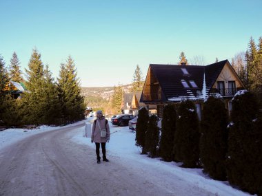 Geleneksel ahşap evler arasındaki karlı dağ yolunda yürüyen bir kadın gezgin.