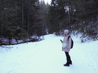 Çam ormanlarıyla çevrili karla kaplı bir dağ yolunda duran bir kızın tam boy portresi..