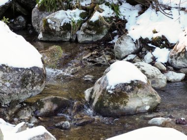 High angle shot of water rushing between frozen rocks in a winter mountain forest.
