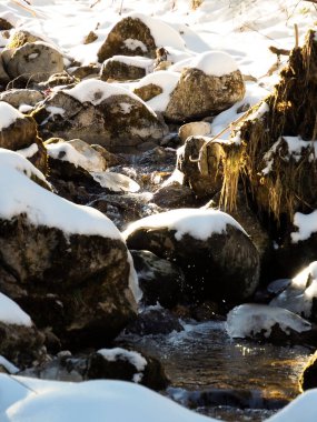 Açık dere suyunun detaylı görüntüsü donmuş kayalar ve derin kış karları arasında akıyor..