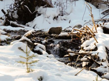 Açık bir kış deresinde kayaların ve karın üzerinden akan temiz suyun yakın çekimi..