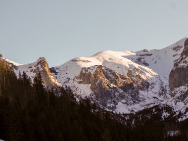 Güneşli kayalık dağ zirvesi kısmen karla kaplı yumuşak mavi gökyüzüne karşı