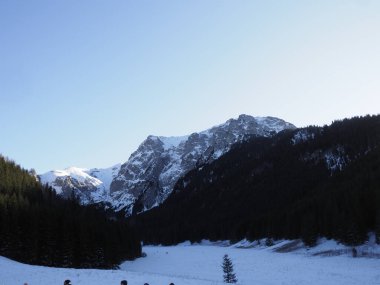 Kış mevsiminde açık mavi bir gökyüzünün altında görkemli kar manzaralı dağ zirveleri.