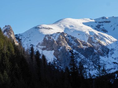 Kayalık bir dağ sırtının yakın çekimi dramatik gölgeler ve açık mavi gökyüzünün altında taze kar.