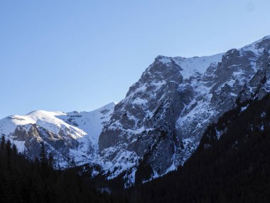 Keskin kar kaplı dağ zirvelerinin alçak açılı görüntüsü açık mavi kış gökyüzüne ulaşıyor..