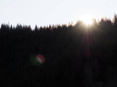 Güneş ışınları, kış günbatımında dağın karanlık tepelerinde parlıyor..