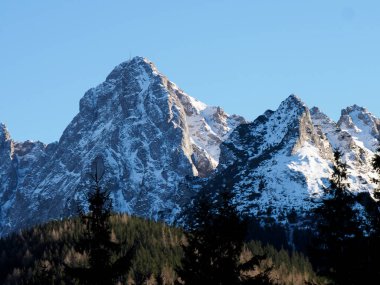 Keskin karla kaplı dağ tepeleri, parlak kış güneşinin altında koyu mavi gölgeler..