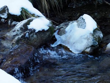 Kış nehrinin hızlı akan suları buzla kaplı büyük kayaların arasından akıyor.