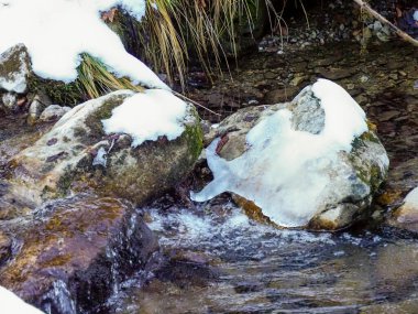 Karlı kayaların arasından akan, altın günbatımı ışığıyla dağ manzarası