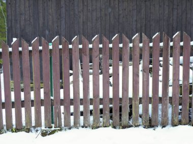 Binanın önünde beyaz karlar içinde duran uzun tahta çitler.