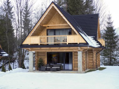 Geleneksel ahşap ev balkonlu ve kışın kar altında taş sütunlu.