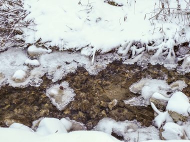 Küçük dağ nehri kış ormanlarında kısmen buz ve karla kaplıdır.