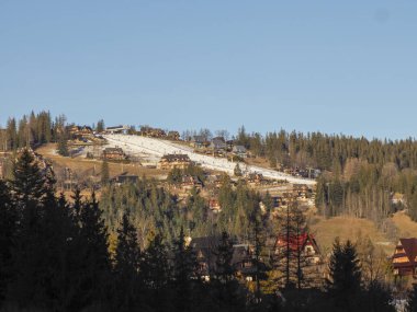 Dağ kayak pistleri ve açık gökyüzünün altındaki ahşap evler manzaralı.