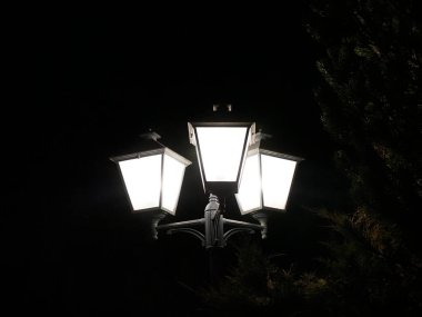 Karanlık bir gökyüzüne karşı izole edilmiş üç lamba ile sokak feneri.