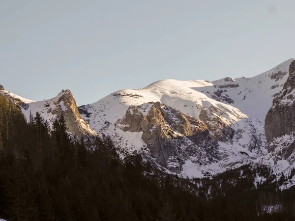 Güneşli kayalık dağ zirvesi kısmen karla kaplı yumuşak mavi gökyüzüne karşı