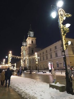 Varşova 'daki aydınlanmış Kutsal Haç Kilisesine doğru yürüyen insanları gece görüşü