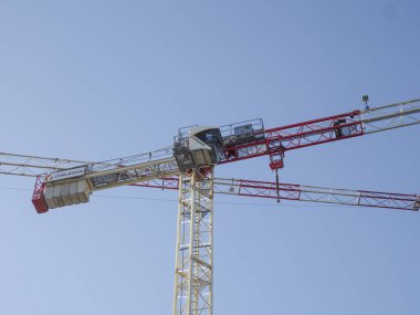 Beyaz ve kırmızı bölümleri olan endüstriyel vinç açık mavi gökyüzünün altında çalışıyor.