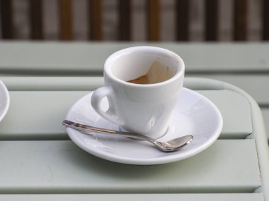 Kafedeki açık yeşil ahşap bir masada beyaz bir fincan espresso kahvesi.