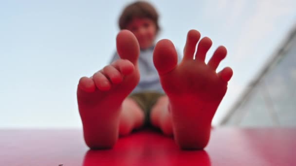 Garçon joue avec ses doigts sur ses pieds assis sur le toit rouge d'une maison d'enfants fermer — Video