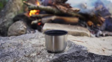 Kamp ateşinin önünde sıcak çay olan metal bardak. Yavaş çekim görüntüleri