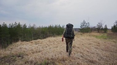 Sırt çantalı genç adam gündüz vakti ormanda yürüyor, ağır çekimde. 